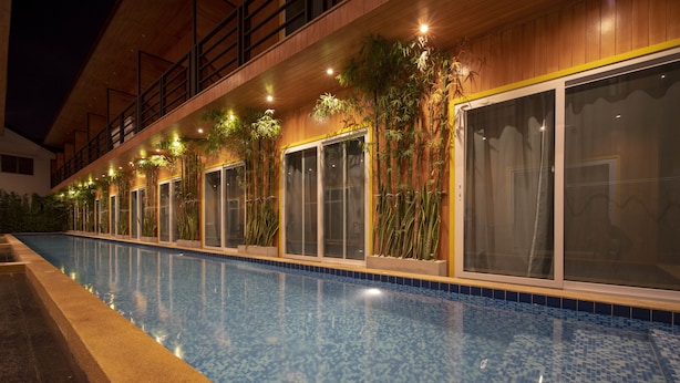 Une piscine dont le bord est revêtu de carreaux, entourée d’une terrasse en bois et agrémentée de plantes en pot.