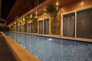 Ein Swimmingpool mit einer gefliesten Kante, umgeben von einer Holzterrasse und Kübelpflanzen.