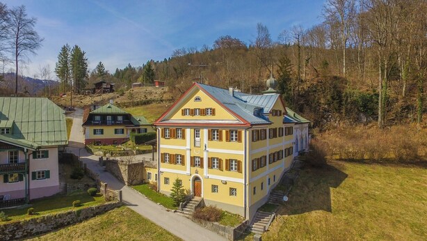 Ein mehrgeschossiges Gebäude mit einer symmetrischen Fassade, einem zentralen Eingang und einer Treppe, die zum Haupteingang führt.