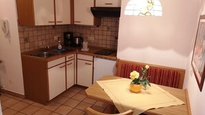 Eine kompakte Küche mit weißen und hölzernen Schränken, einer Kaffeemaschine und einem Essbereich mit Tisch für zwei Personen.