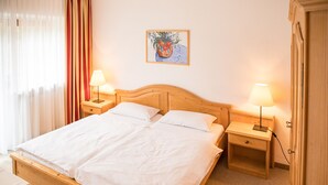 Ein ordentlich bezogenes Doppelbett mit weißen Leinen, zwei Nachttische mit Lampen, ein Bild an der Wand und ein Fenster mit Vorhängen.