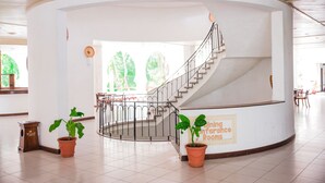 Amplio espacio interior con una escalera curva, plantas en macetas e indicación de salas de comedor y conferencias.