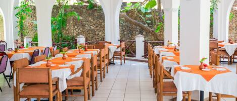 A restaurant with multiple tables and chairs, arranged in a spacious indoor area with natural light and stone walls.