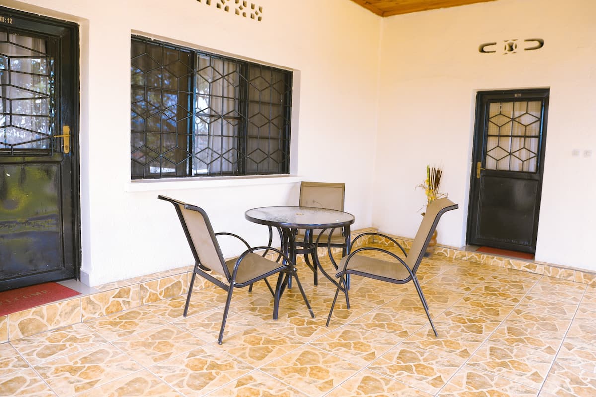 Une pièce avec un sol carrelé, une table ronde entourée de chaises et deux fenêtres dotées de grilles en métal.