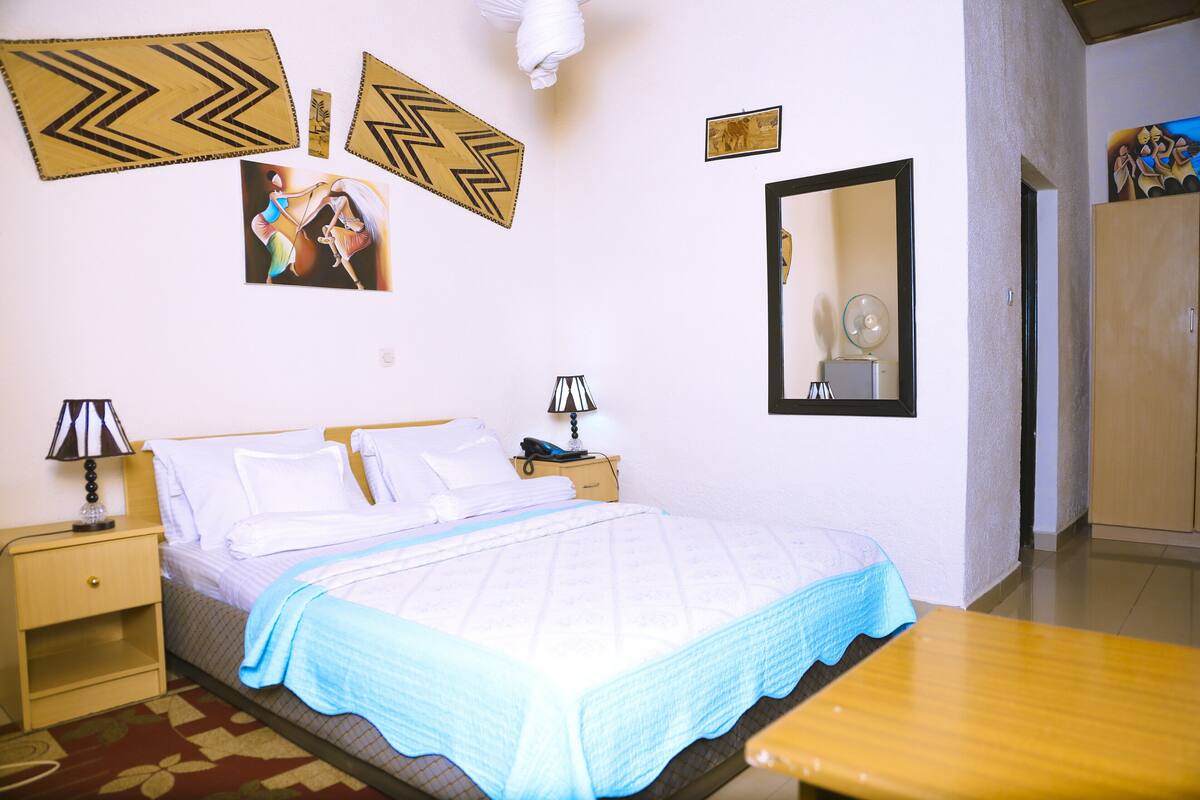 Une chambre à coucher bien rangée, avec un lit, des tables de chevet, un miroir et des éléments décoratifs accrochés au mur.