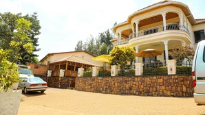 A large house with a balcony, a stone wall, and a parked car. - Step Town Hotel (Kigali)