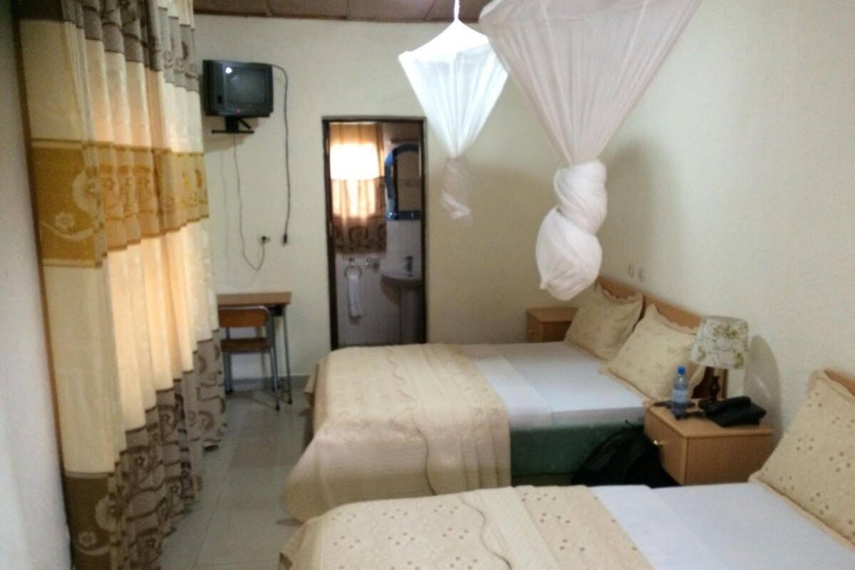 Une chambre d’hôtel avec deux lits, une télévision, une table de chevet avec une lampe et une moustiquaire au-dessus des lits.