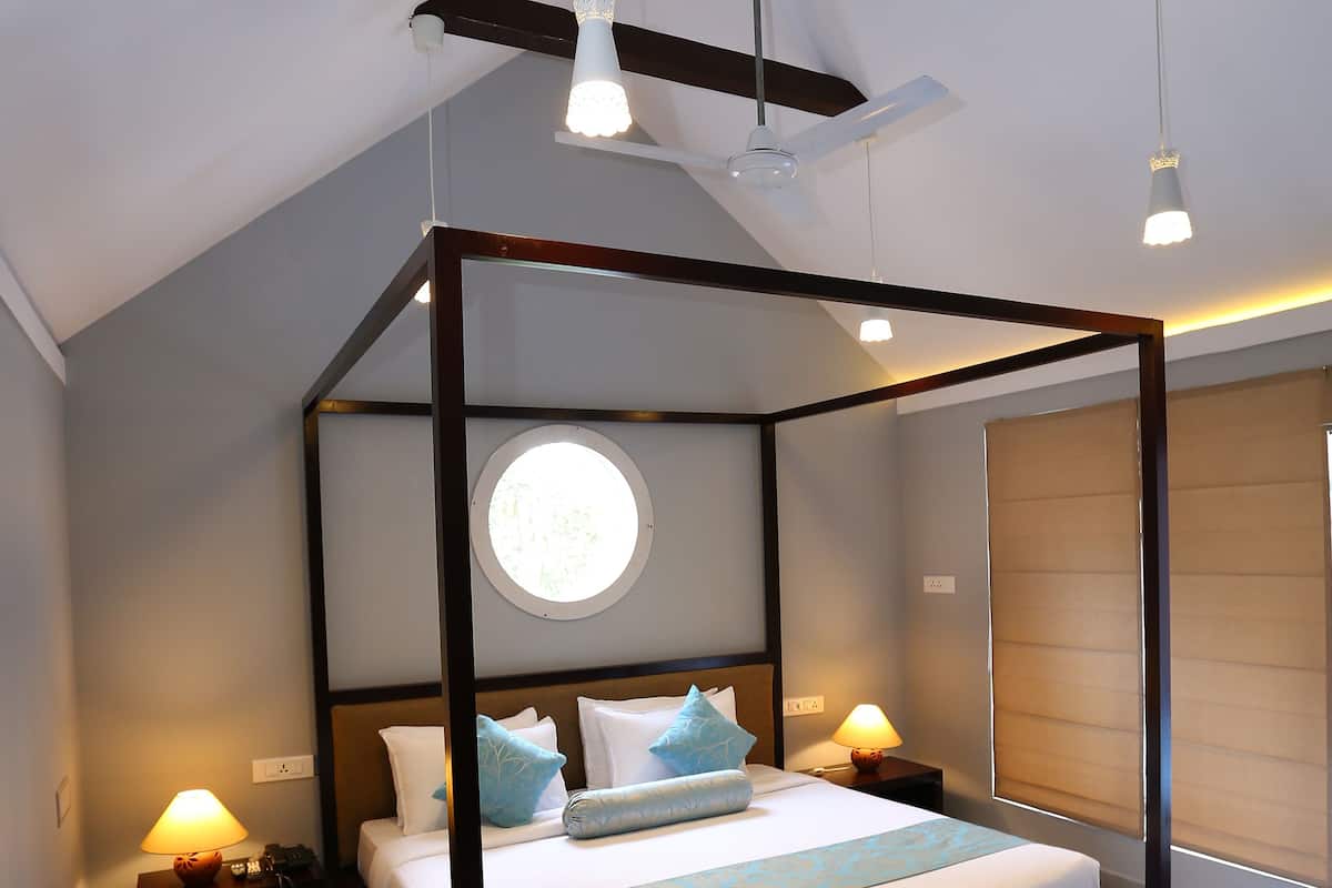 Una cama con dosel, una ventana redonda encima, lámparas de noche y un ventilador de techo.