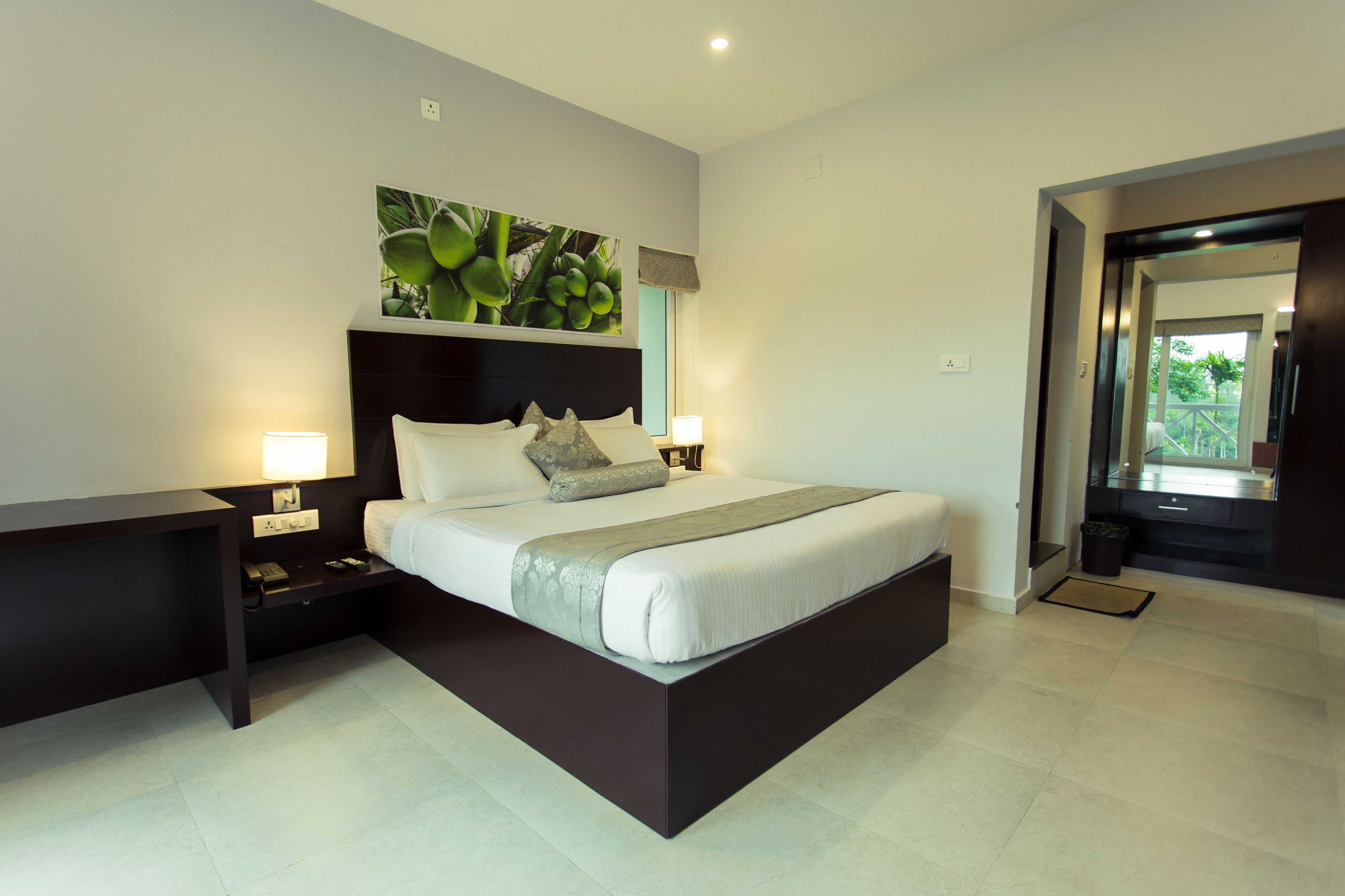 A modern bedroom with a large bed, bedside tables, a nightstand, a headboard, a painting, and a view of the outdoors.