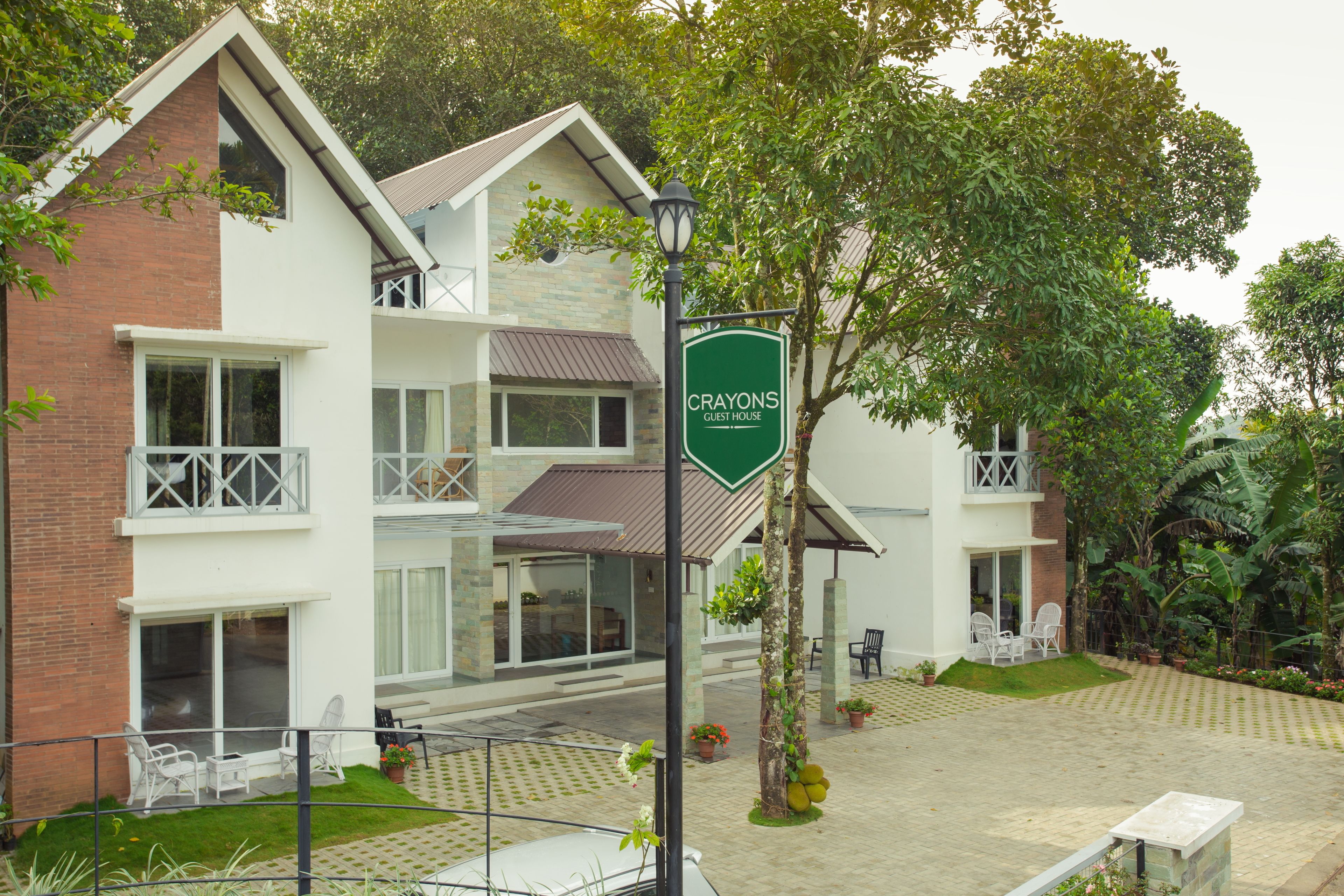 A guest house named Crayons with a brick facade, multiple balconies, and a paved courtyard with outdoor seating.