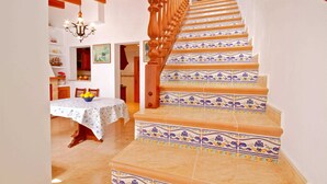 A staircase with ornate wooden balusters and patterned tiles, leading to a dining area with a table set for two and a chandelier.