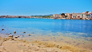 A coastal town with clear blue waters, buildings along the shore, and rocky terrain in the foreground.