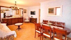 A dining area with a wooden table and chairs, a chandelier, and a television mounted on the wall.