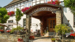 A traditional European-style building with a stone facade, a wooden entrance canopy, and outdoor seating with tables and chairs. - Landgasthof Schneider (Schmallenberg)