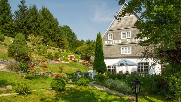 Ein traditionelles Gebäude mit der Aufschrift "GASTHOF SCHINEJAHN", umgeben von üppigem Grün und einem gepflegten Garten.