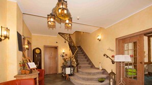 A hotel lobby with a staircase, a red armchair, a wooden door, and a chandelier. - Landgasthof Schneider (Schmallenberg)