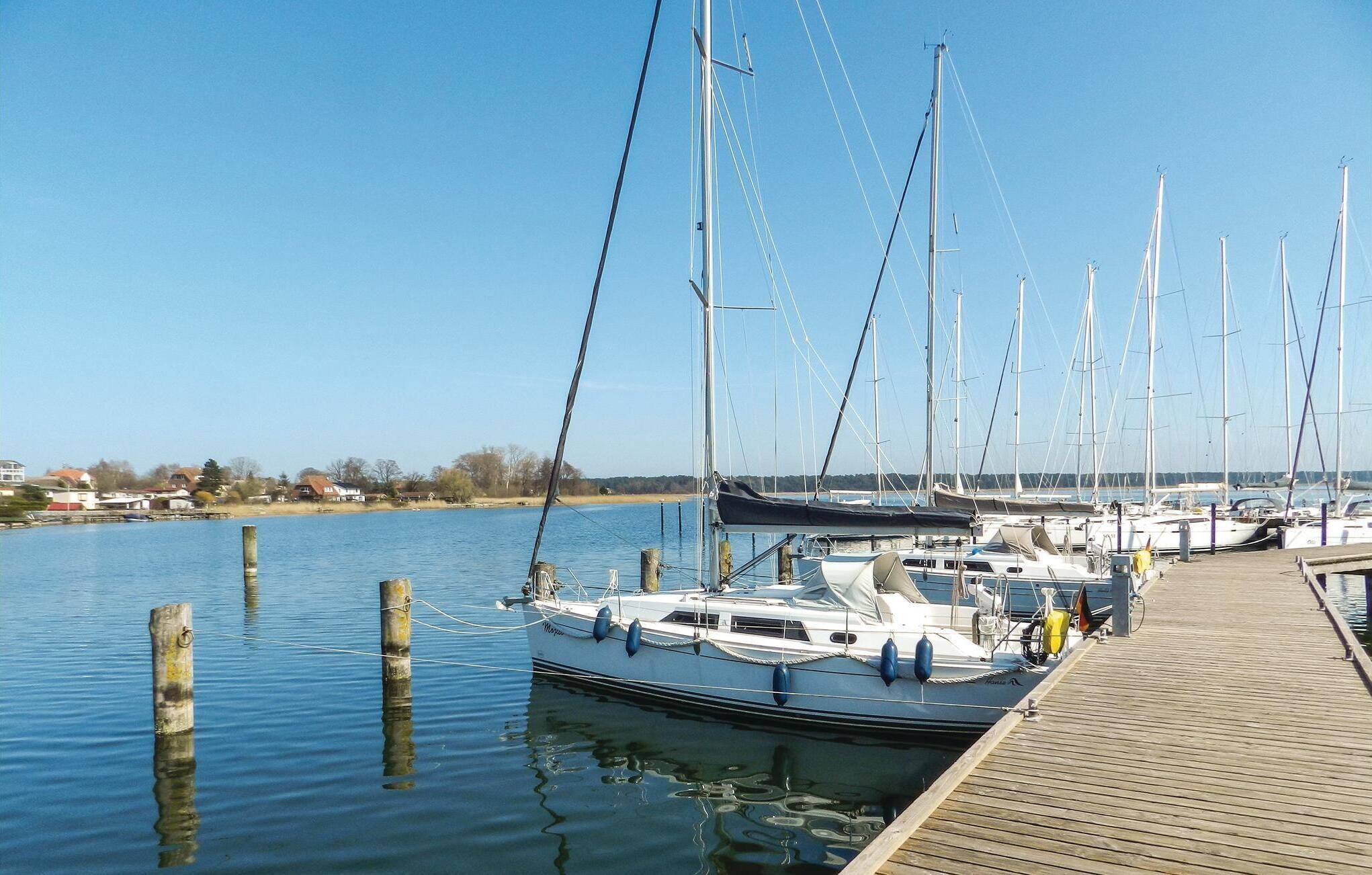 A marina with several sailboats docked, wooden pilings in the water, and a wooden dock.