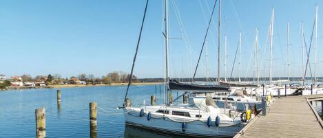 A marina with several sailboats docked, wooden pilings in the water, and a wooden dock.