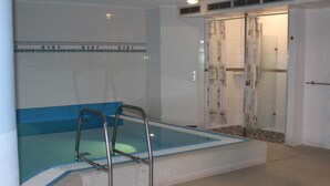 A swimming pool with a blue border, a metal ladder, and a shower area with a glass door. - Residenz Ostseestrand Nr. 11 - Residenz Ostseestrand Whg. 11with balcony (Scharbeutz)