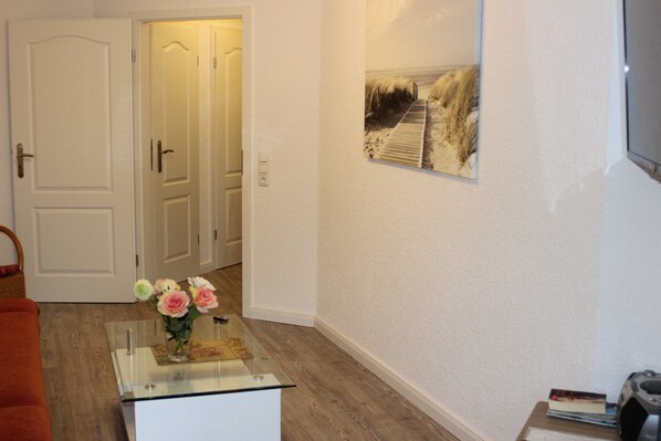 A room with a glass coffee table, a vase with flowers, a framed picture on the wall, and a door leading to another room.