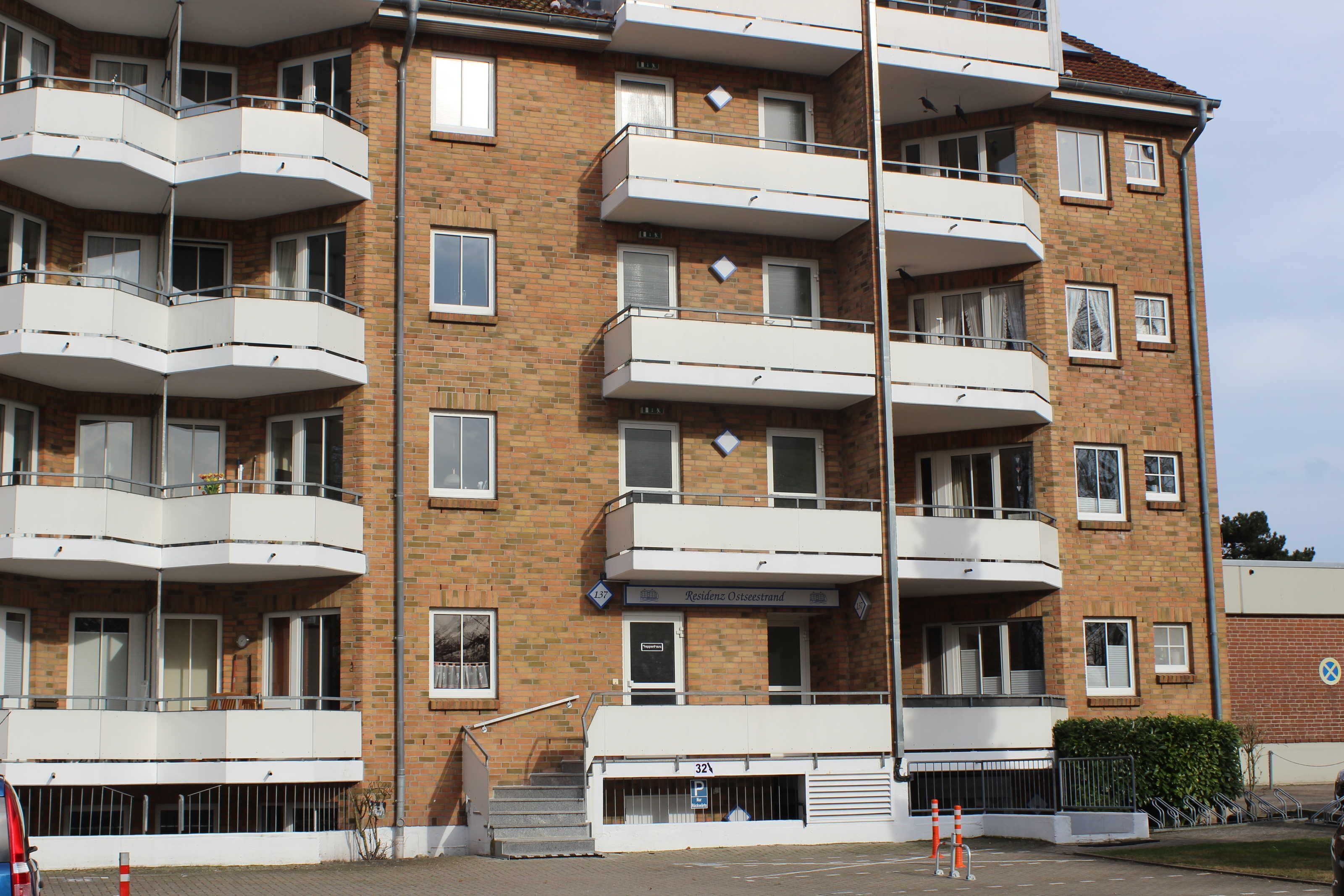 A multi-story residential building with balconies, a sign indicating 'Residences Osteestrand', and a parking area with cones.