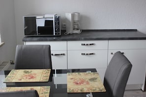 Cozinha compacta com micro-ondas, cafeteira e mesa de jantar com jogos americanos florais.