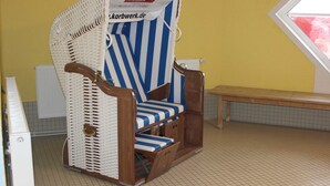A wicker chair with a blue and white striped cushion, a wooden bench, and a radiator in a room with yellow walls and a tiled floor. - Residenz Ostseestrand Nr. 11 - Residenz Ostseestrand Whg. 11with balcony (Scharbeutz)
