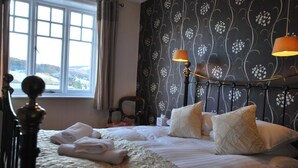Un lit bien fait, avec des serviettes pliées, une tête de lit agrémentée de lampes fixées au mur et une fenêtre avec des rideaux.