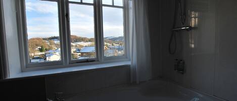 Un baño con una bañera grande, una ventana que ofrece vistas a edificios y colinas, y una zona de ducha.