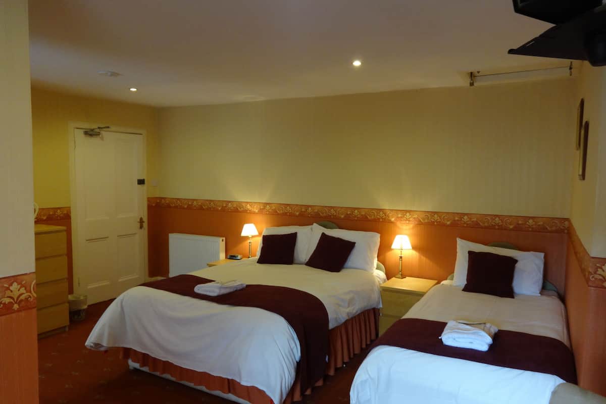 A hotel room with two beds, each with a white comforter and a red blanket. There are two bedside lamps and a door to the left.