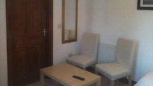 A room with a wooden door, a mirror, two chairs, and a small table with a remote control. - Dumfries Villa (Dumfries)