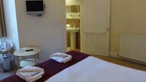 A hotel room with a bed, a TV, a small table with a remote, a trash bin, and a bathroom visible through an open door. - Dumfries Villa (Dumfries)