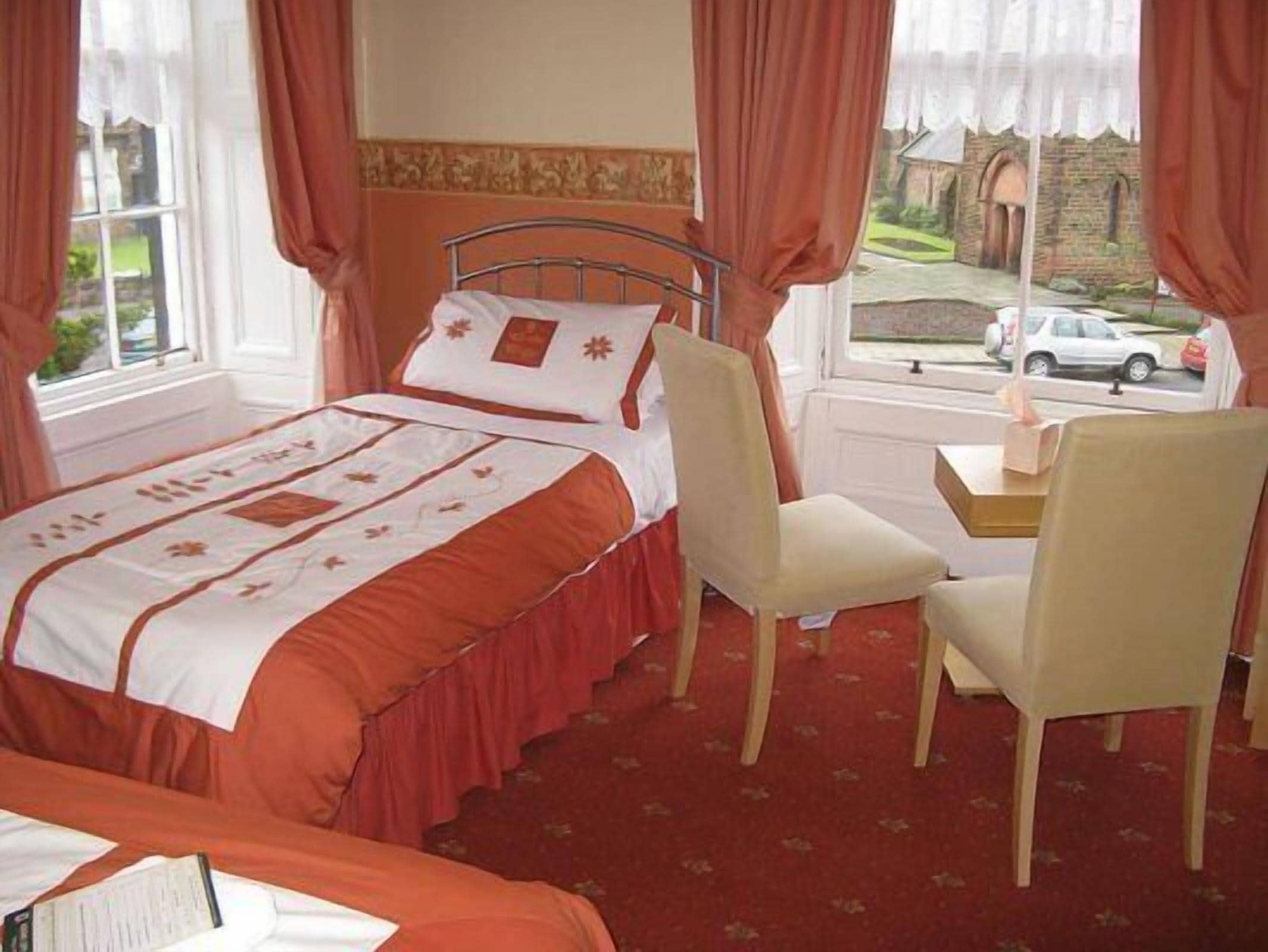 Une chambre d’hôtel avec un lit, une chaise, une fenêtre donnant sur une rue et un immeuble, ainsi qu’une table de chevet avec une lampe.