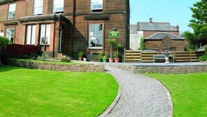A two-story building with a brick facade, a green sign, and a gravel pathway leading to the entrance. - Dumfries Villa (Dumfries)