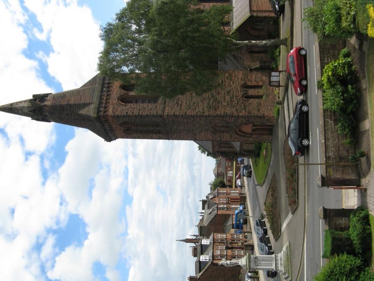A church with a tall tower, a street with cars, and residential buildings.
