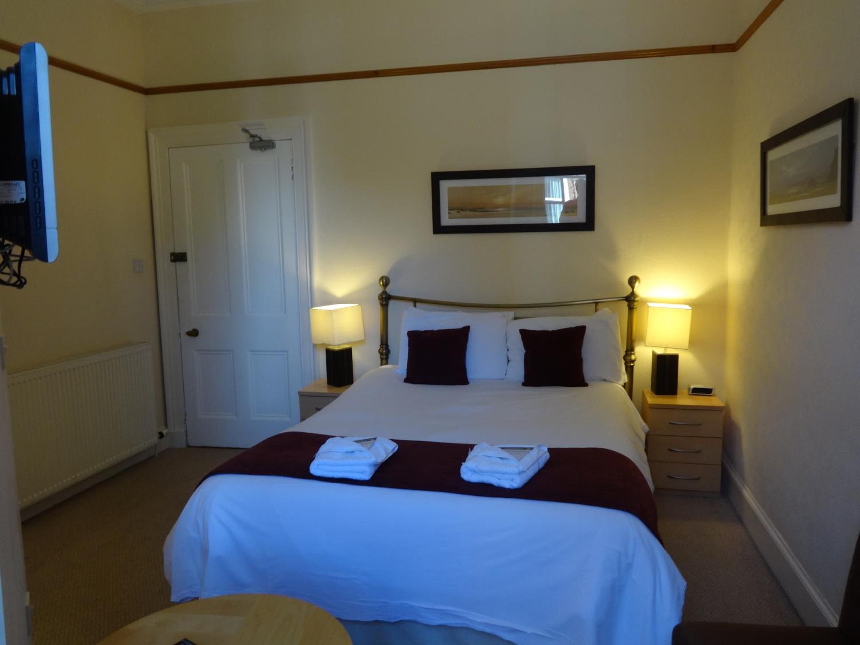 A hotel room with a bed, bedside lamps, a door, and a framed picture on the wall.