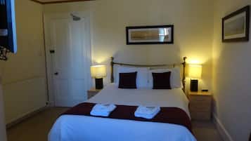 A hotel room with a bed, bedside lamps, a door, and a framed picture on the wall.