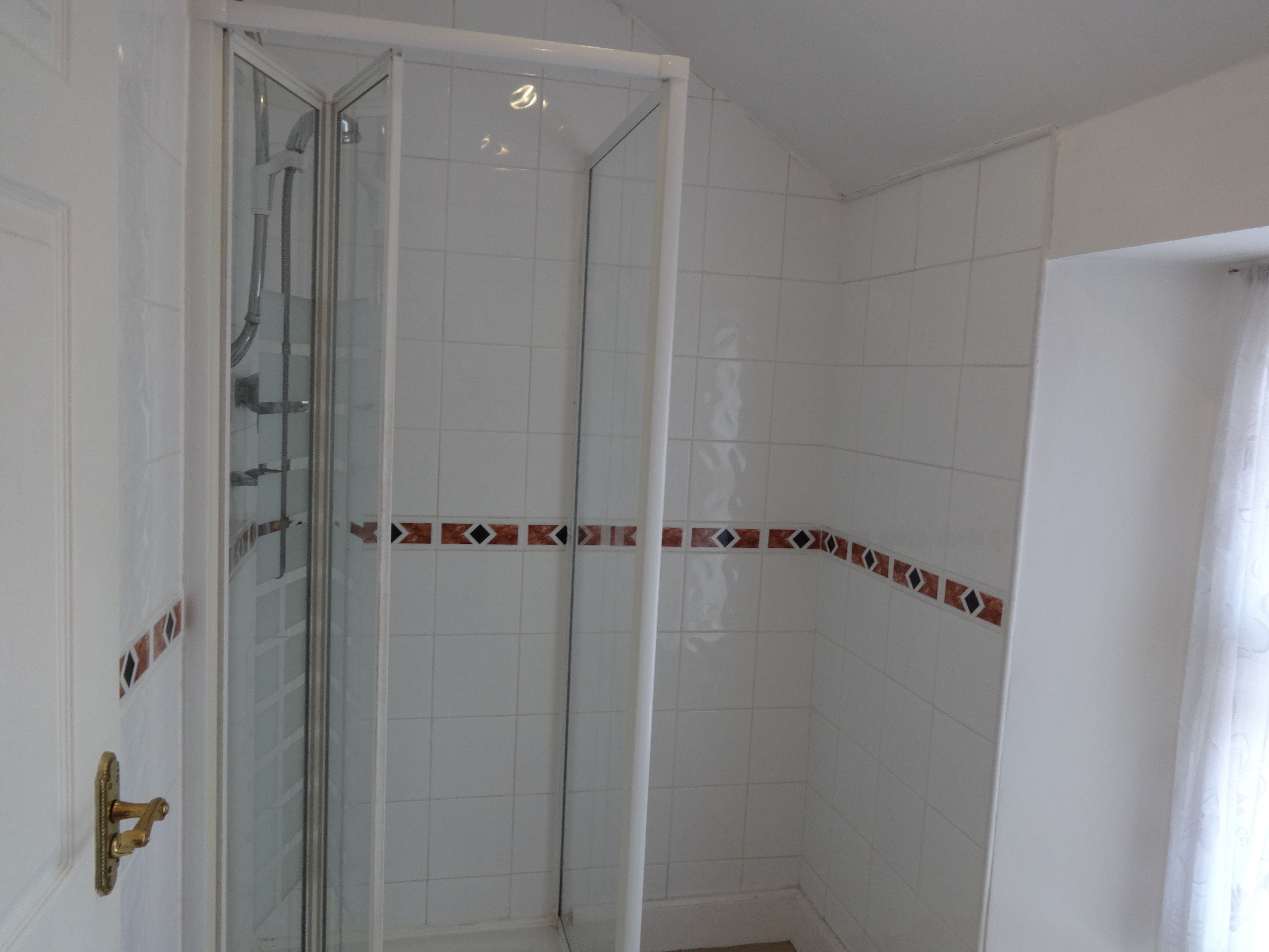A bathroom with white tiled walls, a glass shower enclosure, and a door with a brass handle.