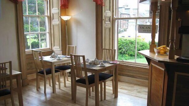 A dining area with wooden furniture, a table set for two, and a view of greenery outside. - Dumfries Villa (Dumfries)