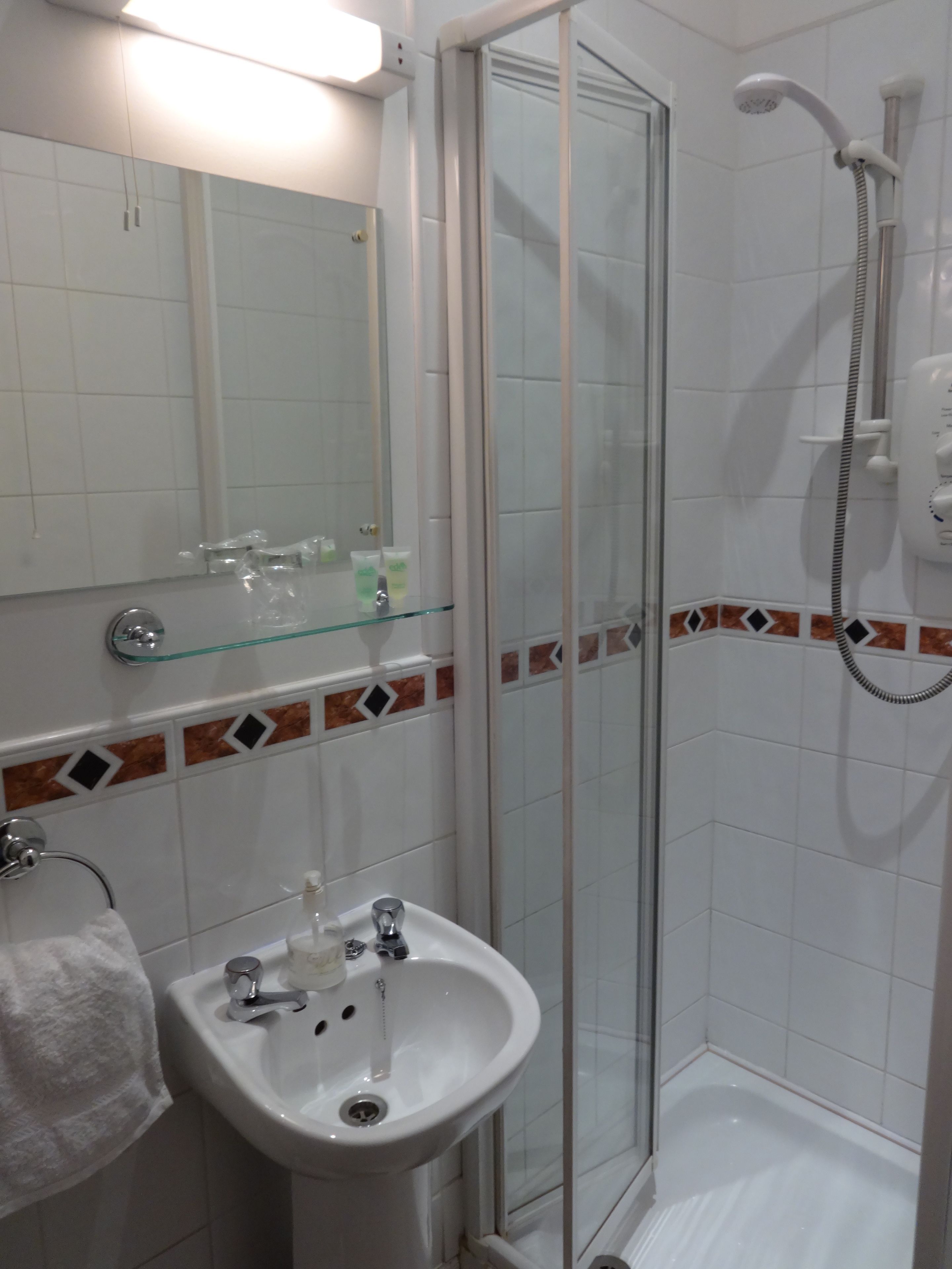 Ein Badezimmer mit Duschkabine aus Glas, einem weißen Waschbecken mit Spiegel darüber und einem Handtuchhalter.
