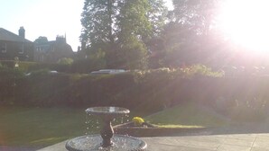 A fountain in a courtyard with a tiled floor and a grassy area with trees in the background. - Dumfries Villa (Dumfries)