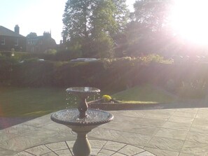 A fountain in a courtyard with a tiled floor and a grassy area with trees in the background. - Dumfries Villa (Dumfries)