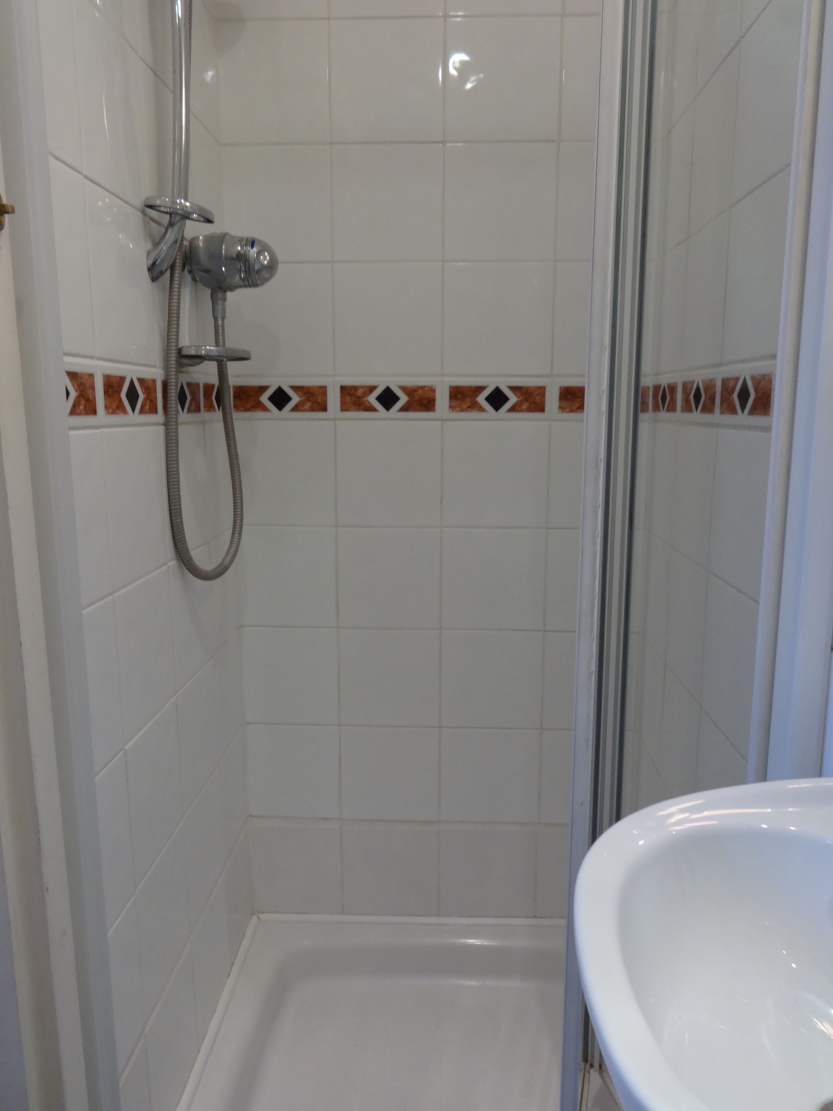 A shower with a glass door, white tiles, and a decorative tile border.