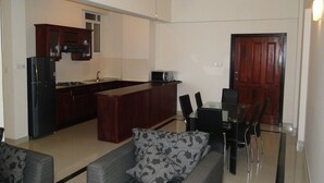 A modern kitchen with dark cabinetry, a central island, and a dining area with a glass table and black chairs. - BRAMA Servizez - Capital Park (Colombo)