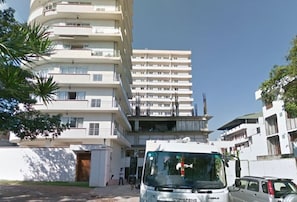A multi-story building with balconies, a parked van, and a clear sky.