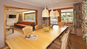 Un espace repas avec une longue table en bois, des chaises en osier et des lampes suspendues.