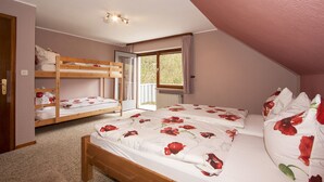 Une chambre avec un lit superposé, un lit simple avec une literie à motifs floraux, une fenêtre avec des rideaux et un radiateur.
