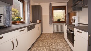 Une cuisine moderne avec des meubles blancs, un carrelage au sol, un four encastré et une fenêtre avec des rideaux.