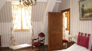 A bedroom with a bed, a chair, a table, and a window with curtains. - Château de la Court d'Aron (Saint-Cyr-en-Talmondais)