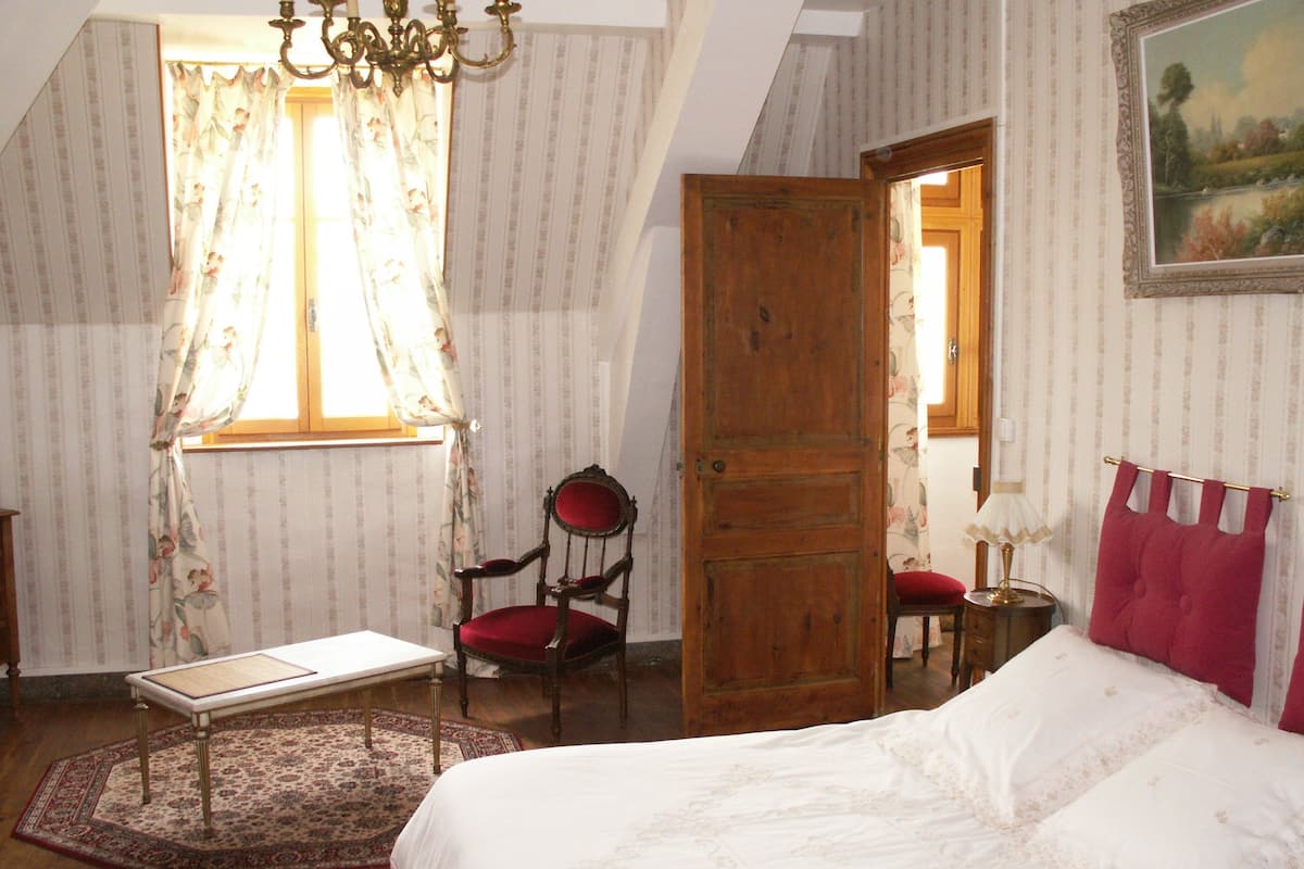 A bedroom with a bed, a chair, a table, and a window with curtains.